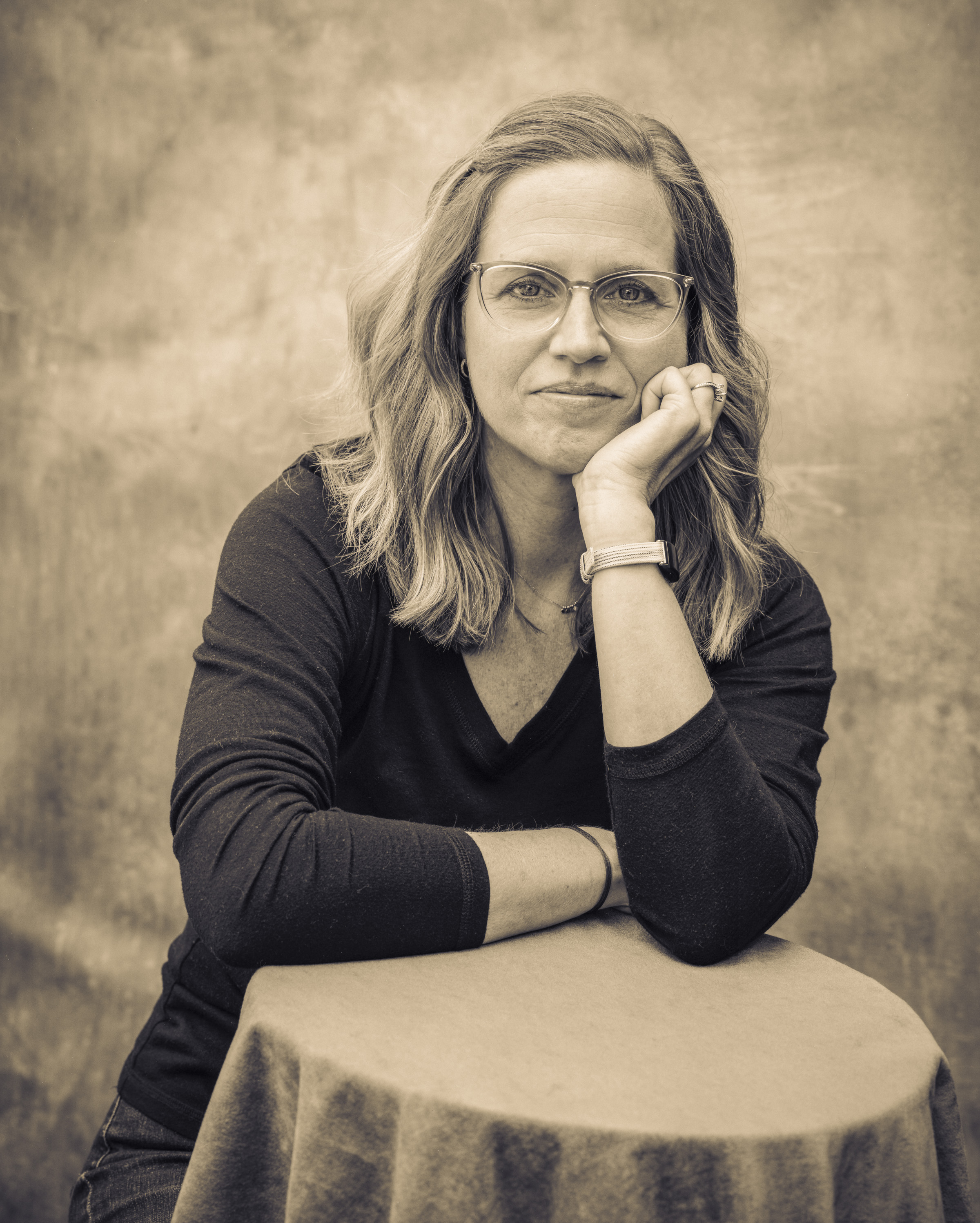 Black-and-white portrait of Kim Morrow, leaning on covered table