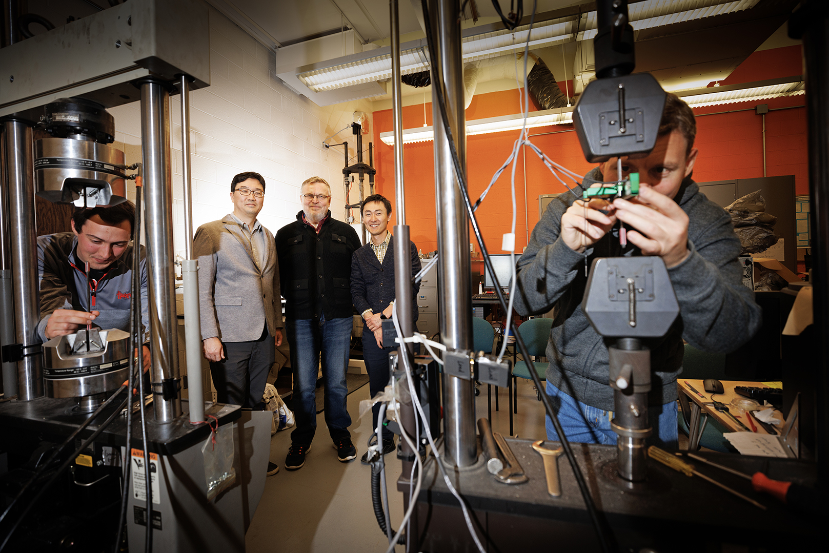 Husker engineers Jongwan Eun (center left), Yuris Dzenis (center) and Seunghee Kim (center right) pose in Dzenis’ lab as Benjamin Bashtovoi (left), a junior mechanical engineering major, and Mikhail Kartashov (right), an engineering graduate student, test carbon-fiber samples. Eun, Dzenis and Kim have received $675,000 from the Department of Energy’s Established Program to Stimulate Competitive Research to investigate how inorganic microfibers can make a more resilient barrier material to im