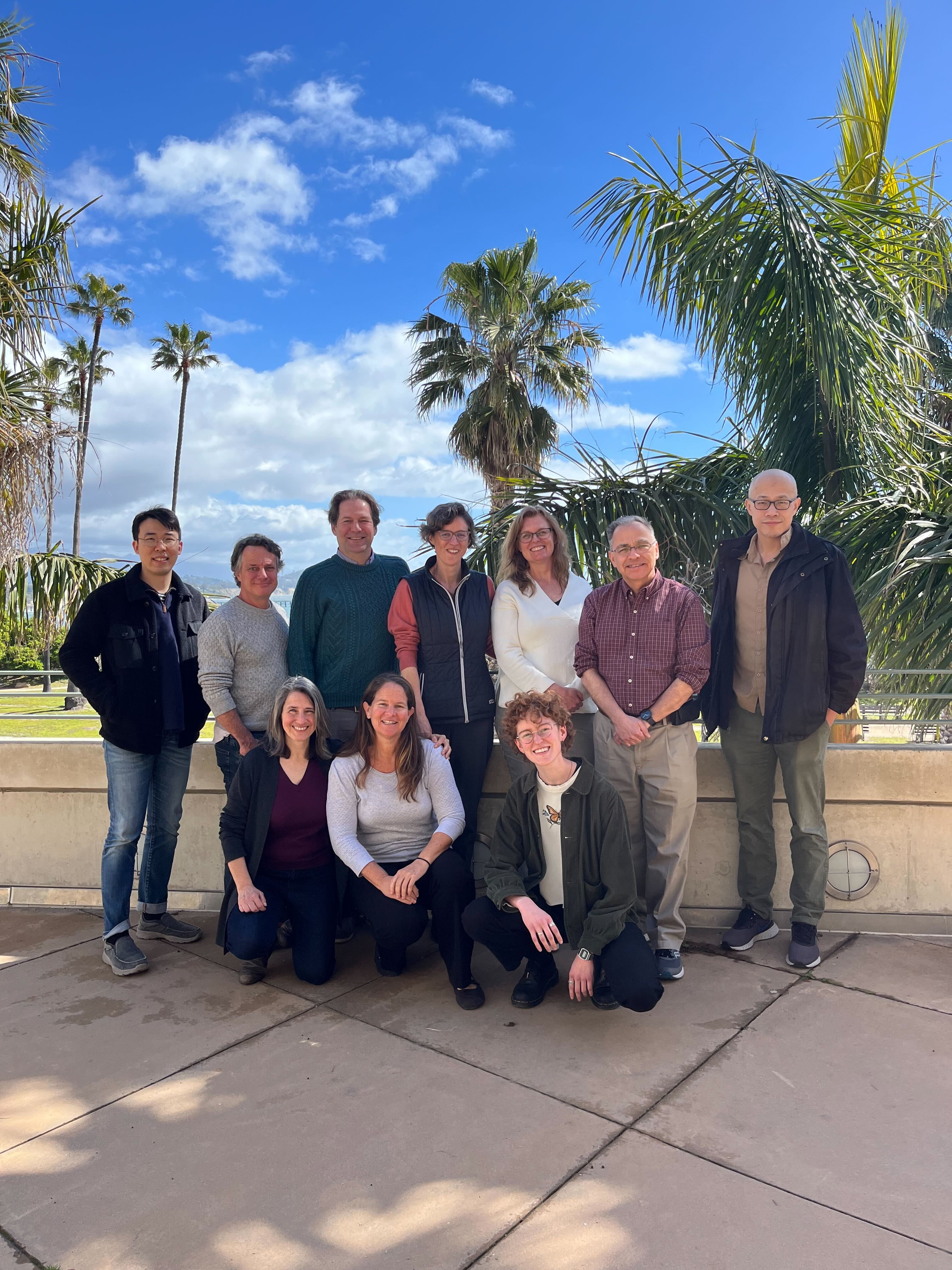 Ten researchers pose in front of palm trees.