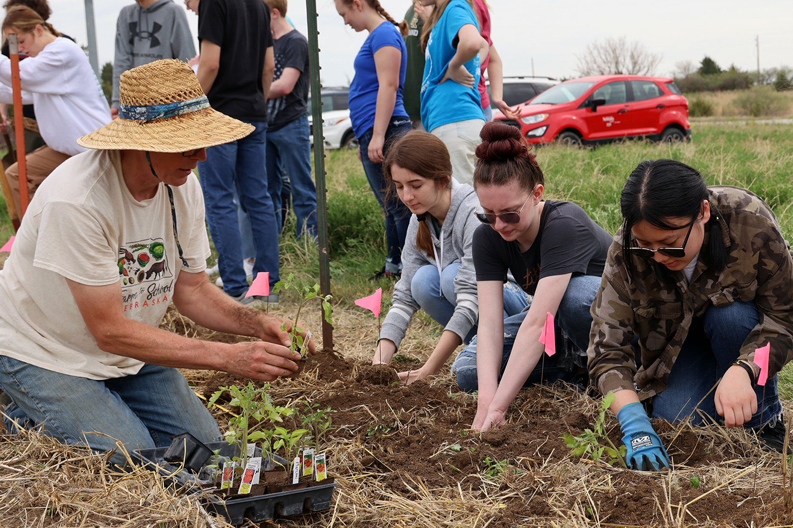 Gary Fehr, owner of Green School Farms in Raymond, shows students from Pius X High School how to plant tomatoes.