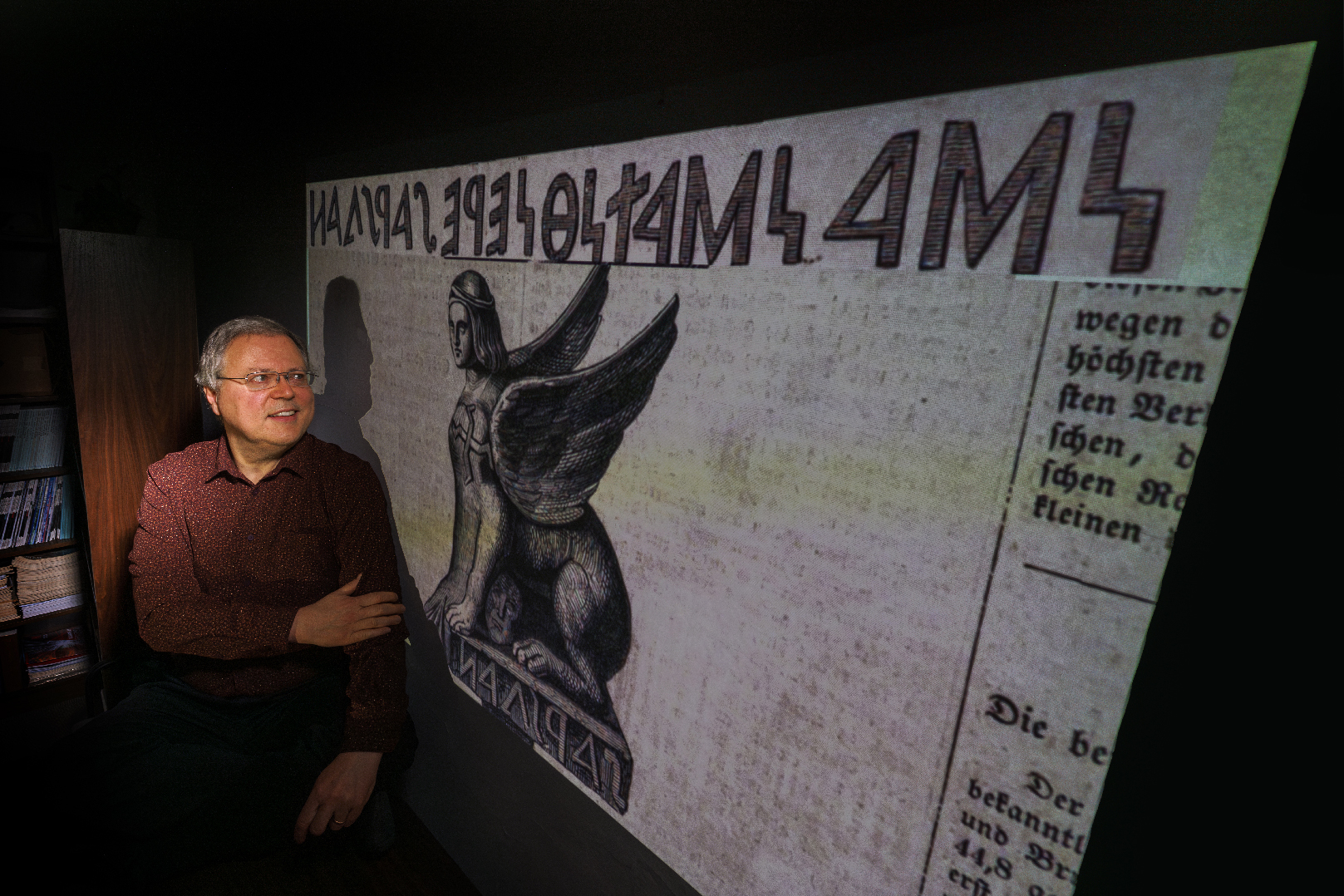 Peter Revesz poses in front of artwork of an ancient sphinx with an inscription that he deciphered.