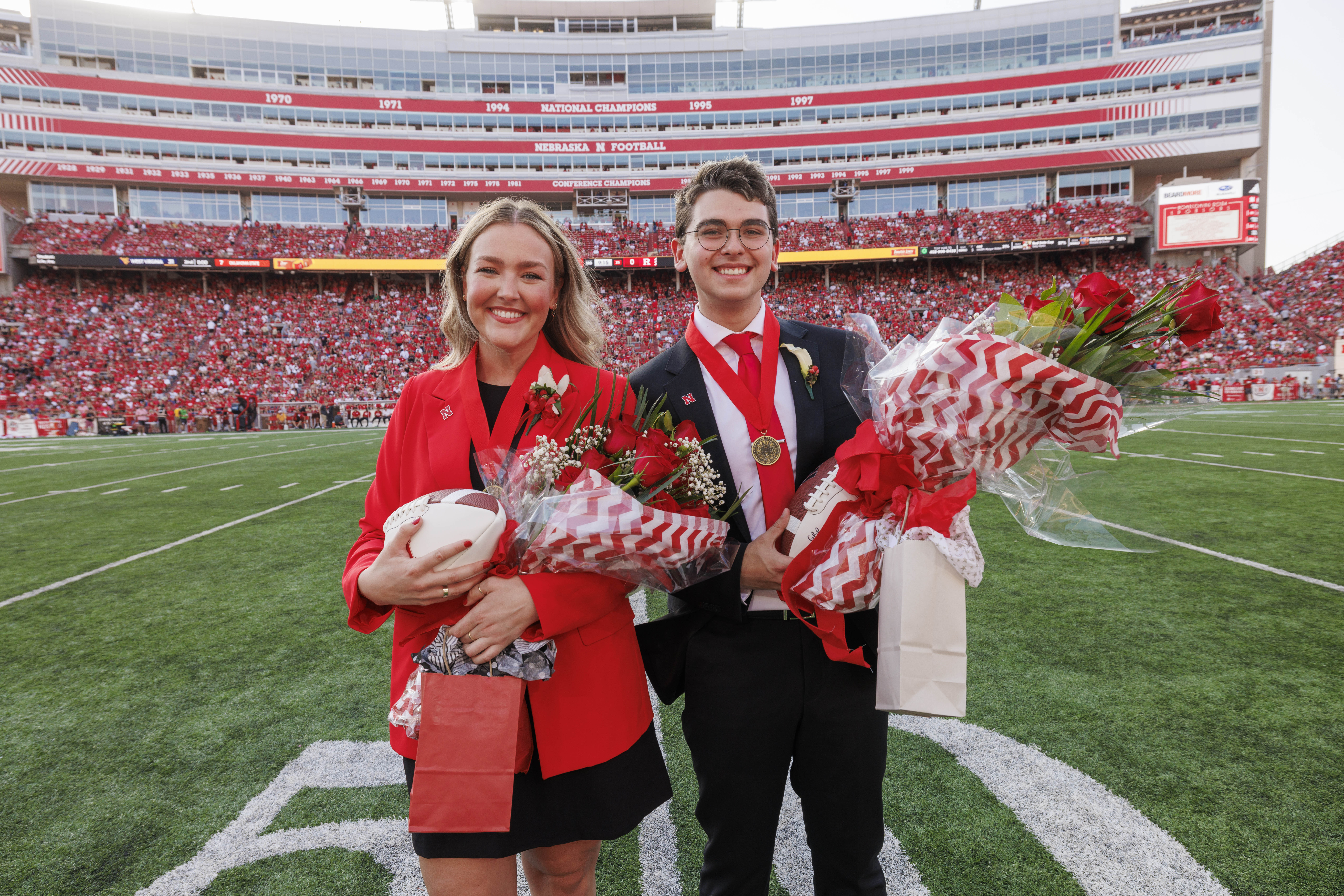 Husker seniors Emmerson Putnam (left) and Jamie Smith pose with footballs, flowers and gift bags on the 50 yard line of Memorial Stadium after being crowned homecoming royalty.