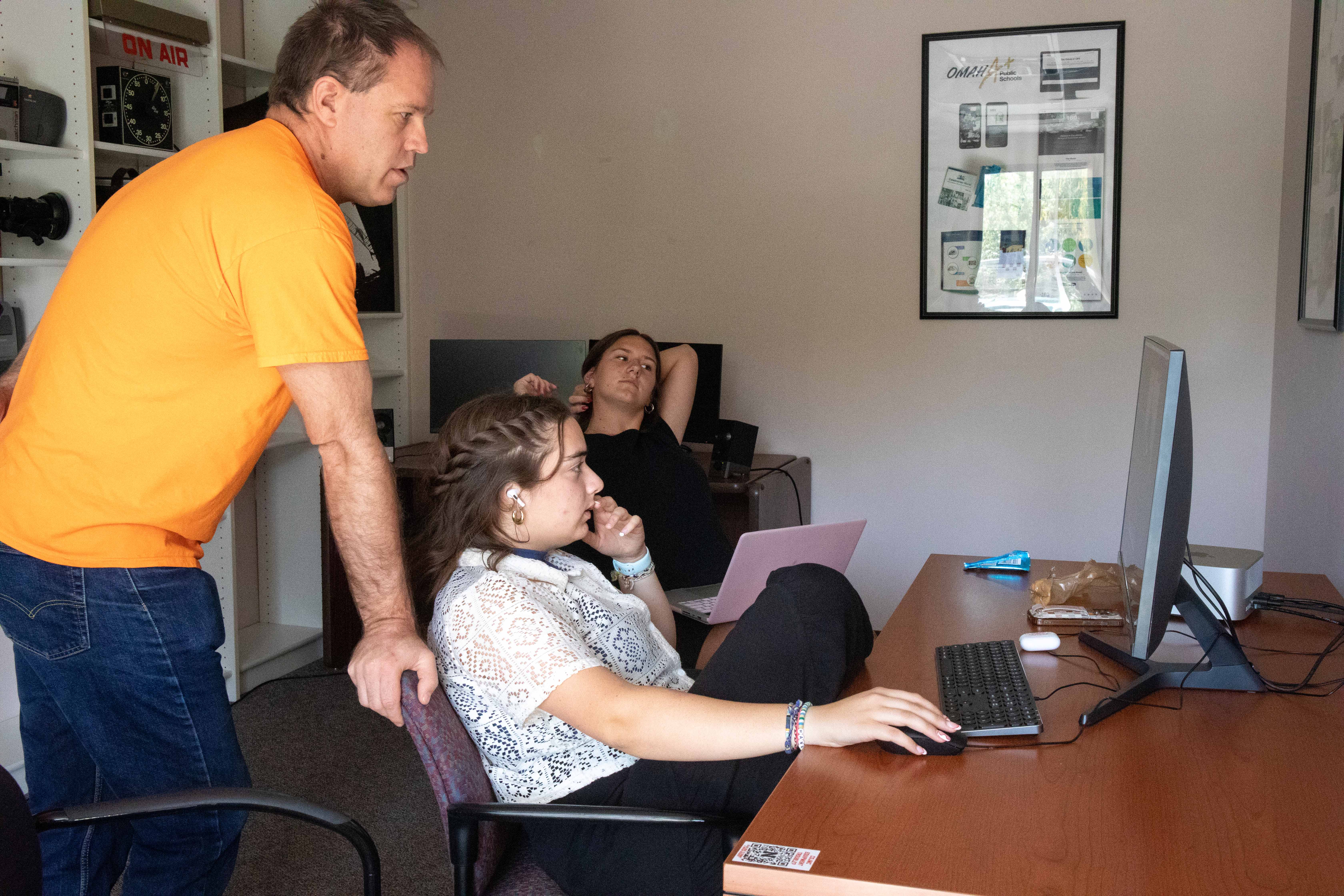 Alan Eno, associate professor of practice in broadcasting, works with Jacht crew members Hana Maddox and Molly Keifer at the Jacht Ad Agency. The three look at a computer monitor, with Eno standing and Maddox and Keifer sitting.