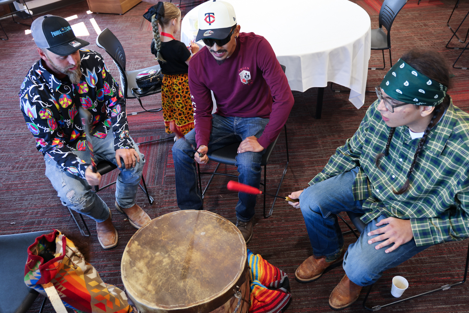 Three young men play a Native drum.