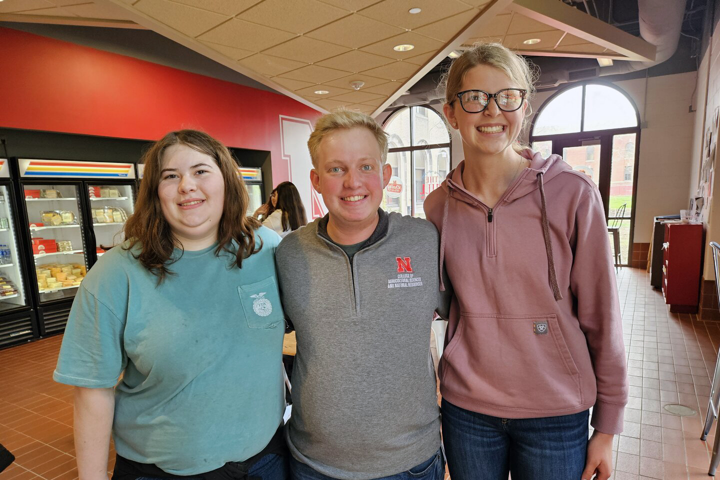 Carie Goodwater (left) and Melany Preister (right), students at Boone Central High School, pose with Brian Mock (center), a Husker student mentor who graduated in May, at the UNL Dairy Store.