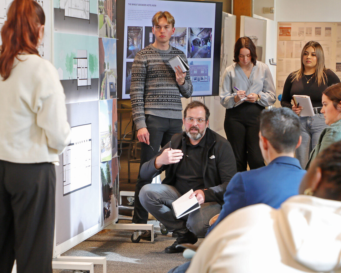 Nate Bicak (center), associate professor of interior design, speaks to a group of seven students in a classroom.