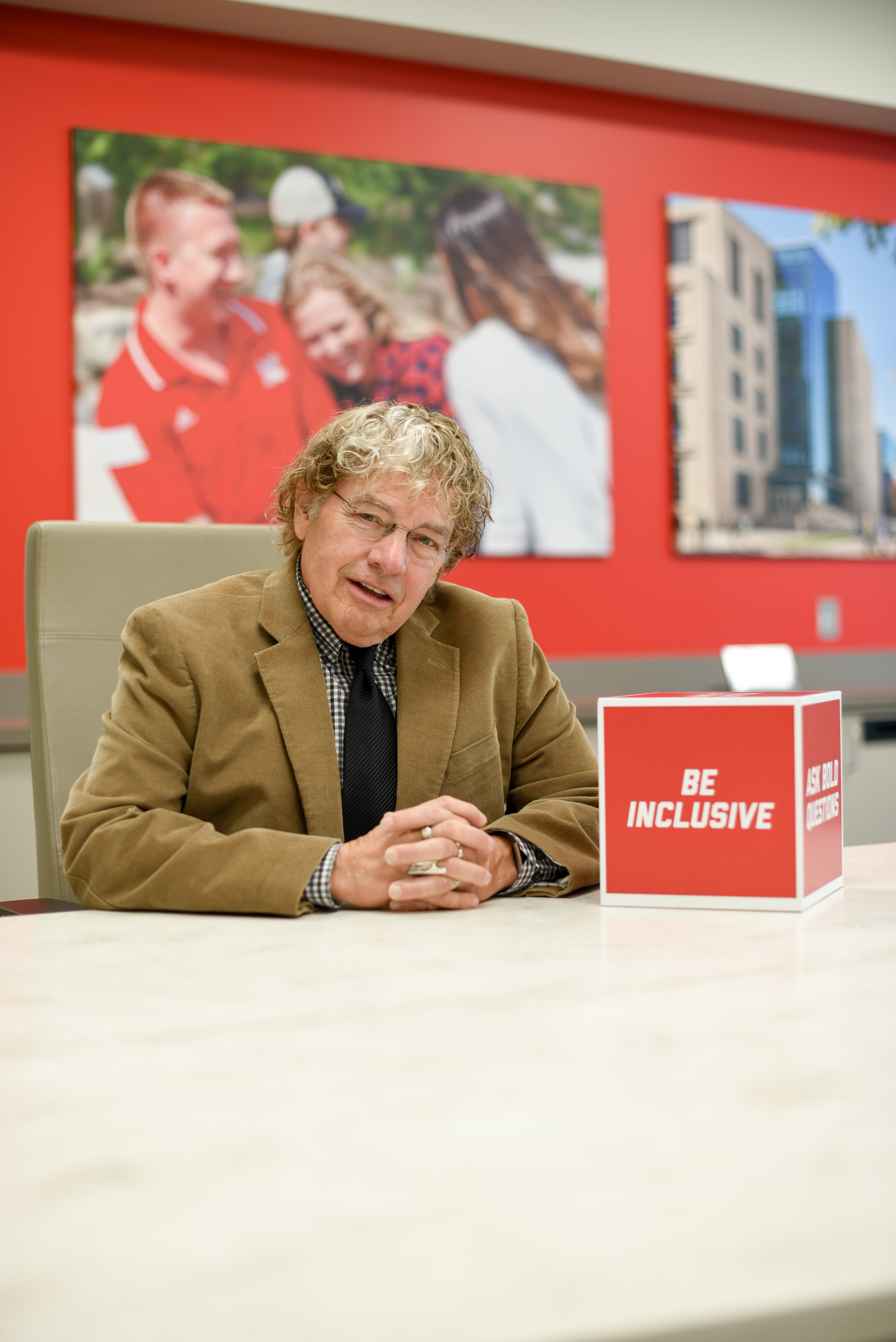 Musician, sound engineer and University of Nebraska–Lincoln alumnus J. E. Van Horne Jr. sits at a table. He is wearing a black-and-white plaid dress shirt, black tie, brown jacket and glasses.