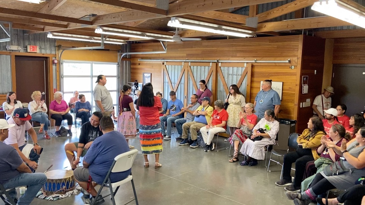 Two dozen or so people sit in a circle playing a traditional Indigenous guessing game called a hand game at the Spring Creek Prairie Audubon Center.
