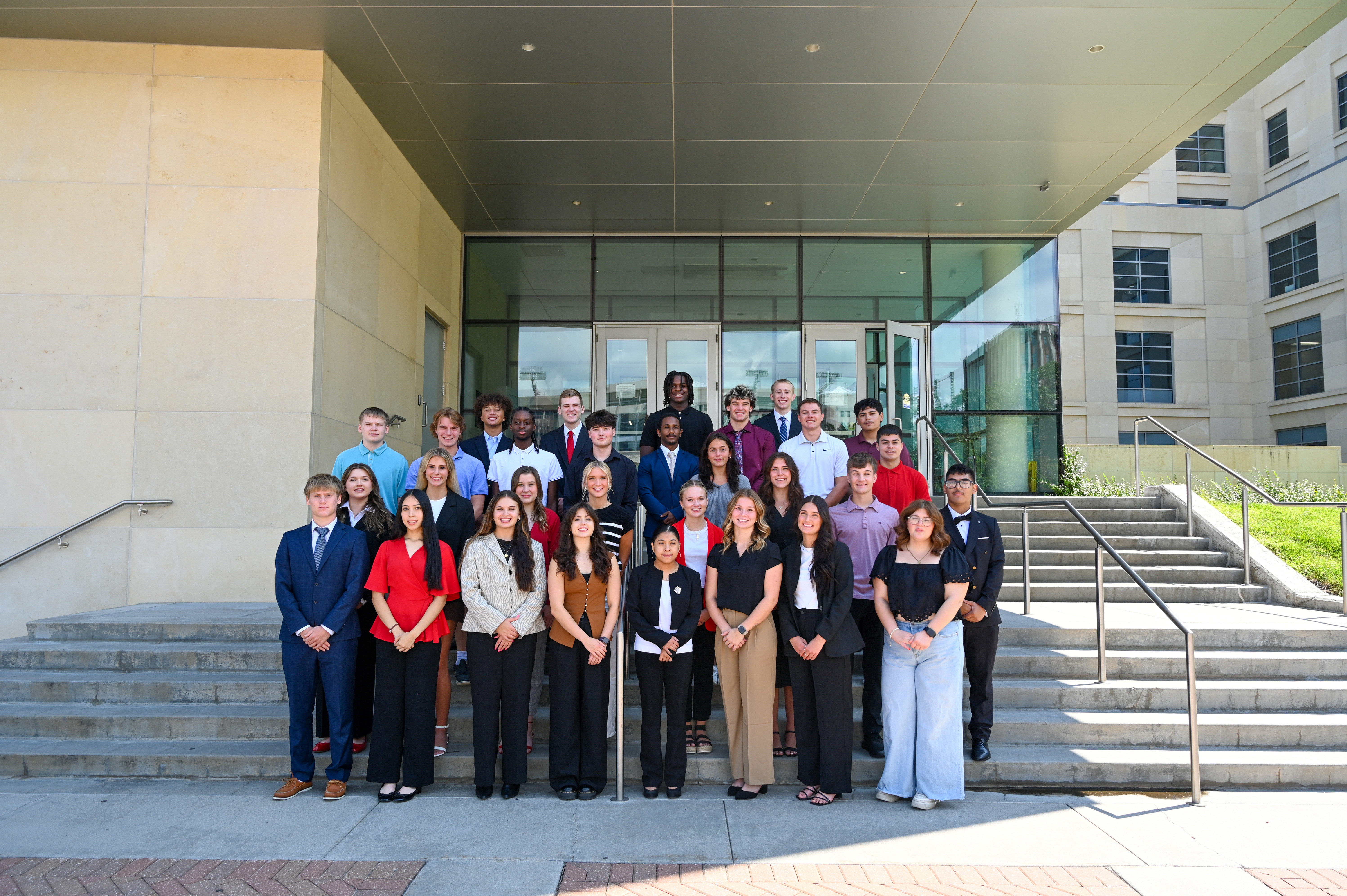 Thirty college students in dress clothes pose for a photo on the west steps of Howard L. Hawks Hall.