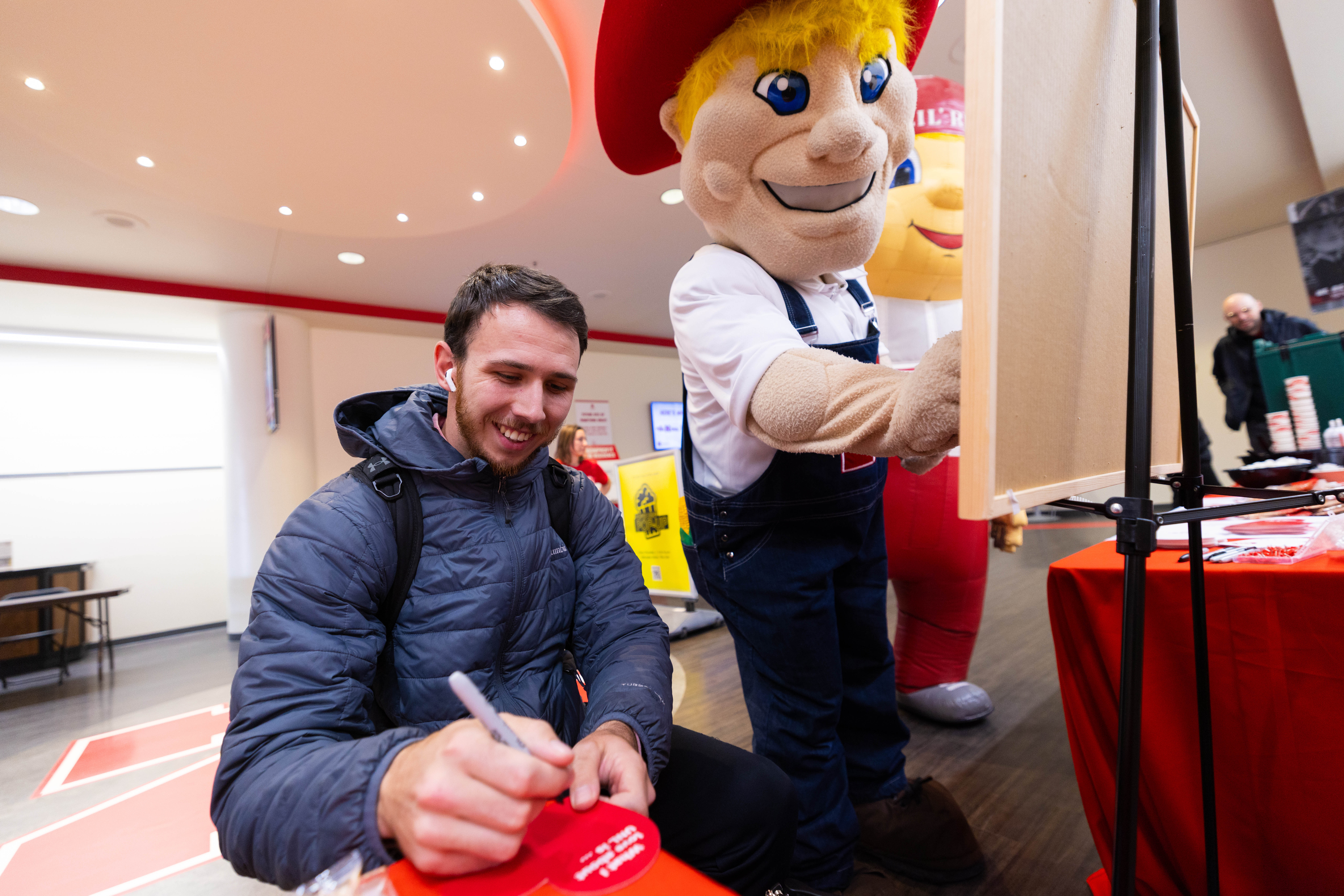 Zac Hartman, a junior mechanical engineering major, writes what he loves about the University of Nebraska–Lincoln on a heart for Glow Big Red. Next to Hartman are mascots Herbie Husker and Lil' Red.