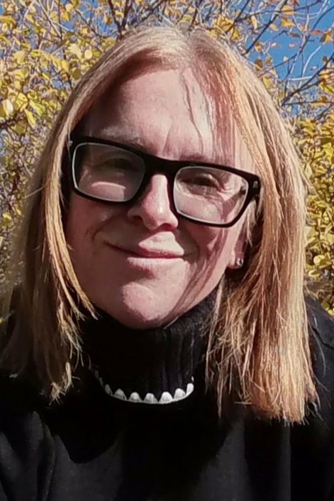 Color portrait of Carol Graham, wearing a black turtleneck and black-framed glasses.