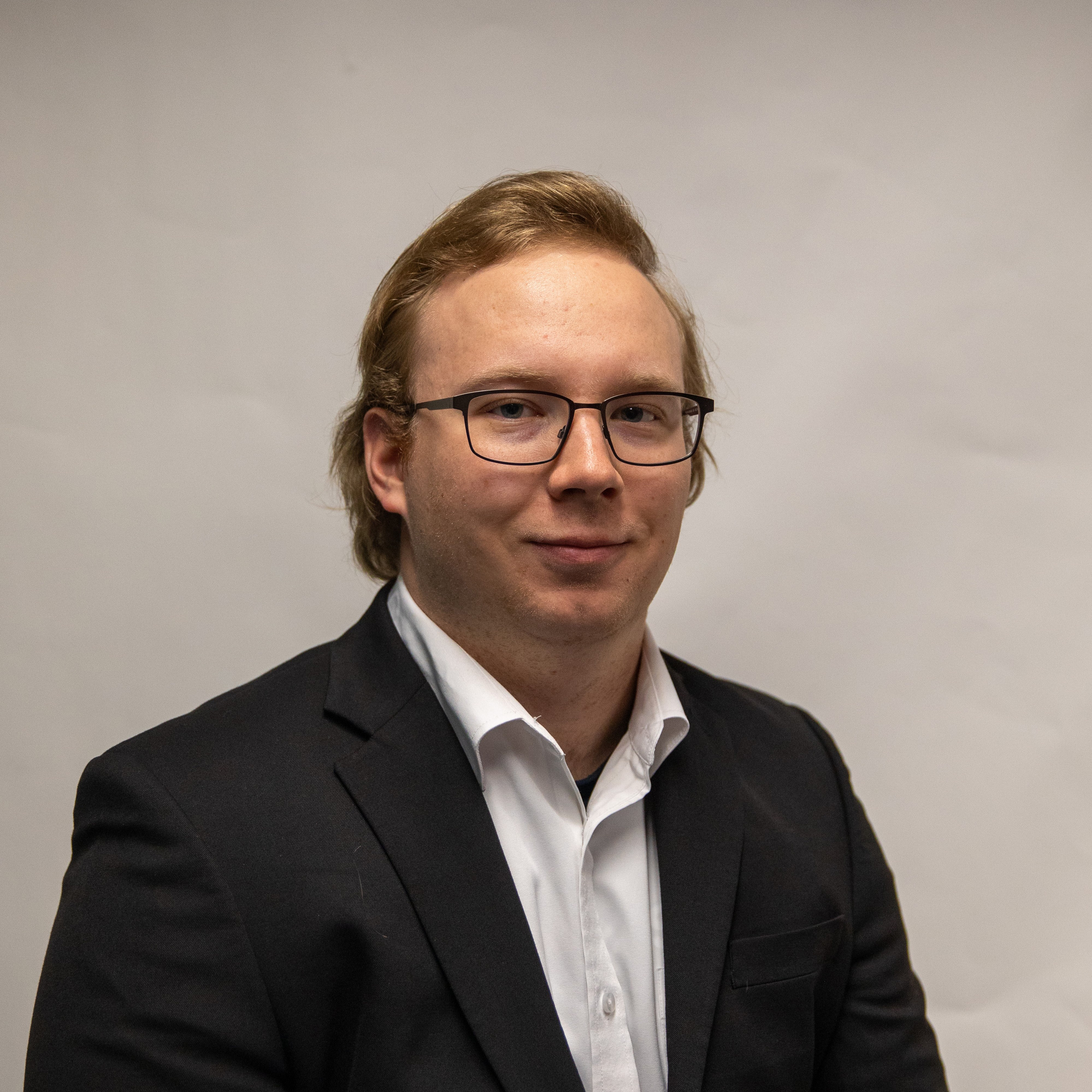 Color portrait of Danny Berg, junior broadcasting and sports media and communication major at the University of Nebraska–Lincoln. He is wearing a black sport coat over a white dress shirt, with glasses.