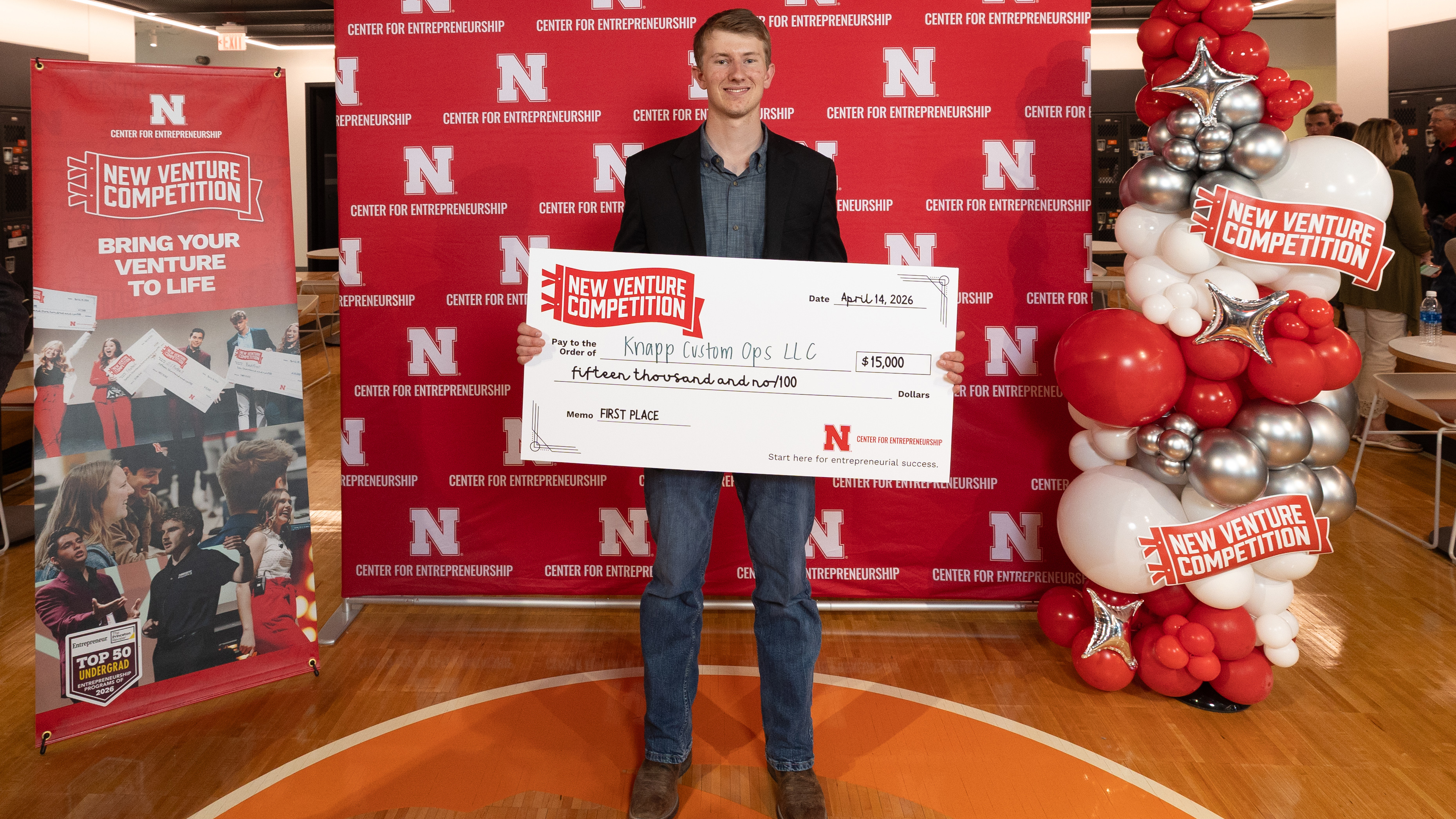 Adam Knapp, a junior agribusiness major from Ord, Nebraska, holds an oversized check for $15,000 in front of a Center for Entrepreneurship backdrop and balloons.
