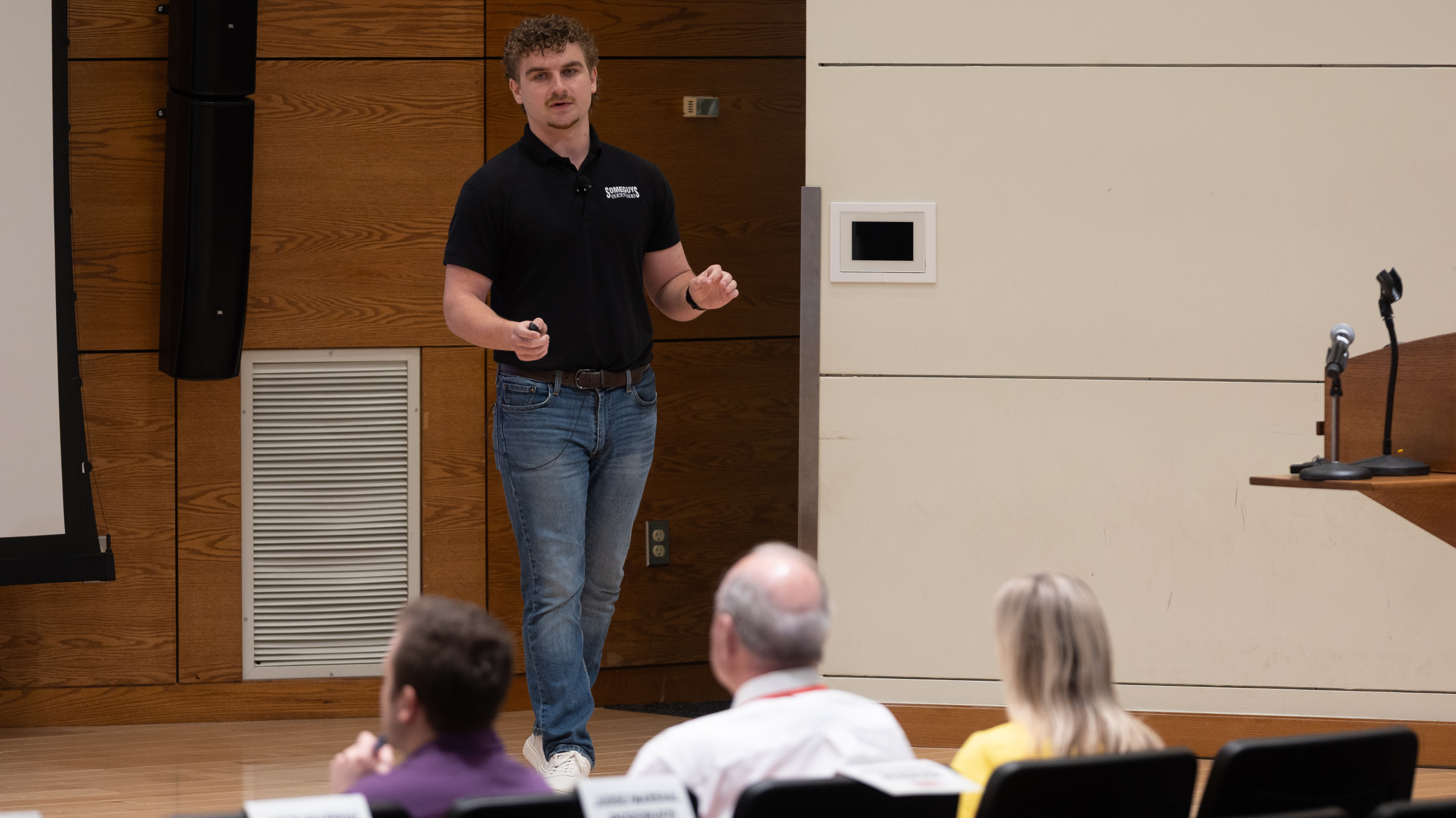 Jackson Donley, a junior Clifton Builders management major from Bloomington, Minnesota, stands on stage, giving a presentation to three judges.