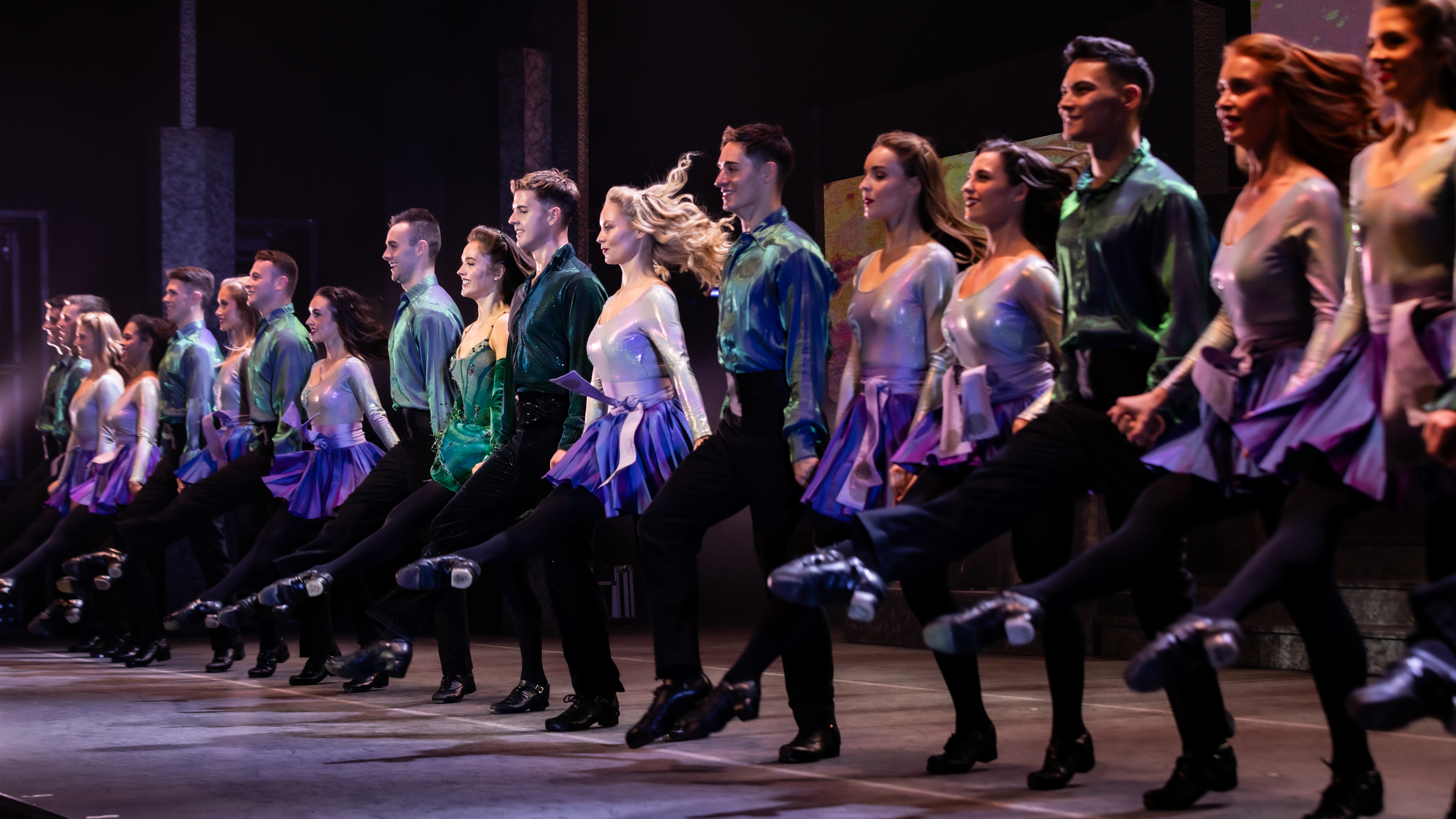 A line of Irish dancers, men and women, perform in Riverdance.