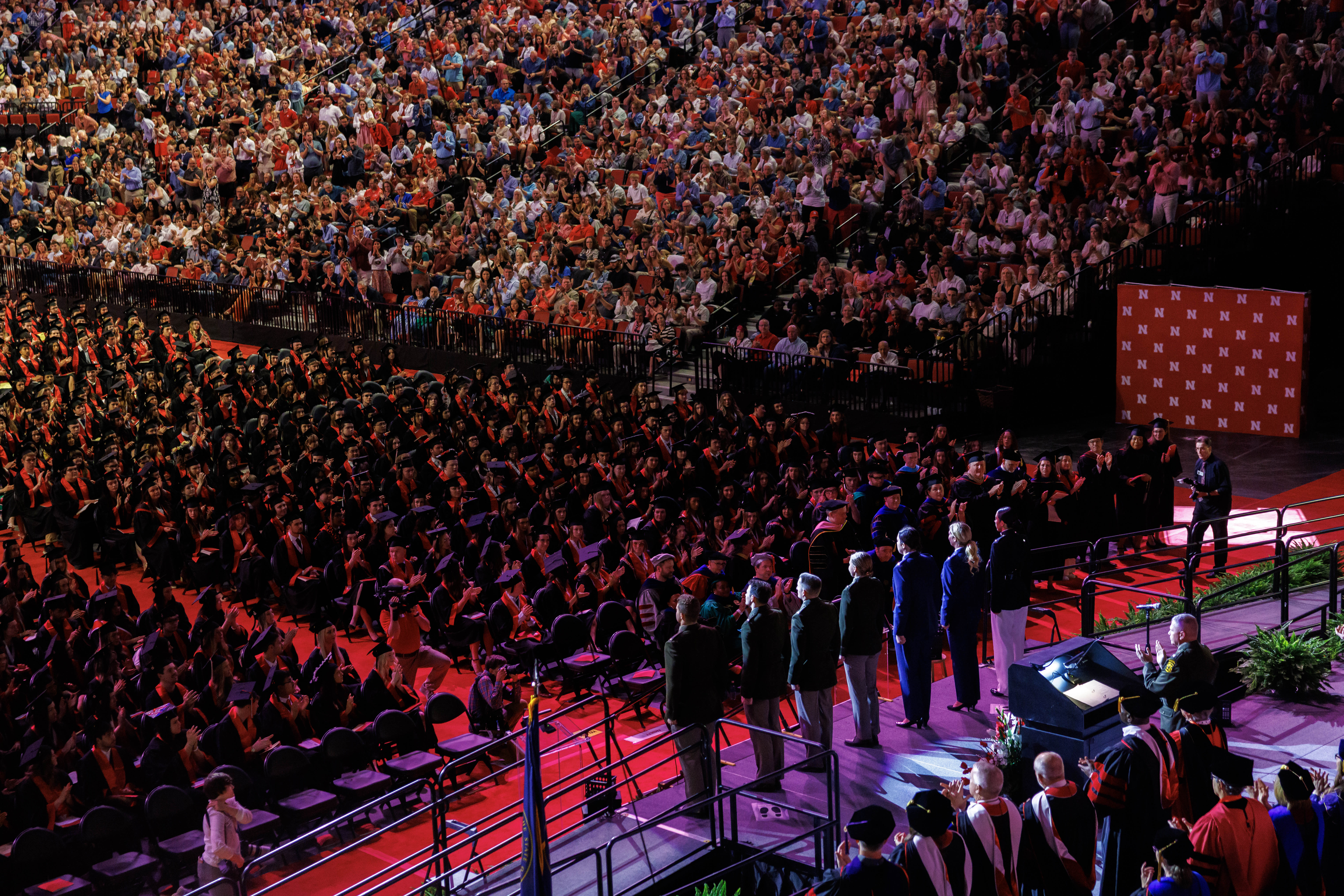 Seven ROTC members in uniform stand onstage at Pinnacle Bank Arena as the audience and their fellow graduates applaud.