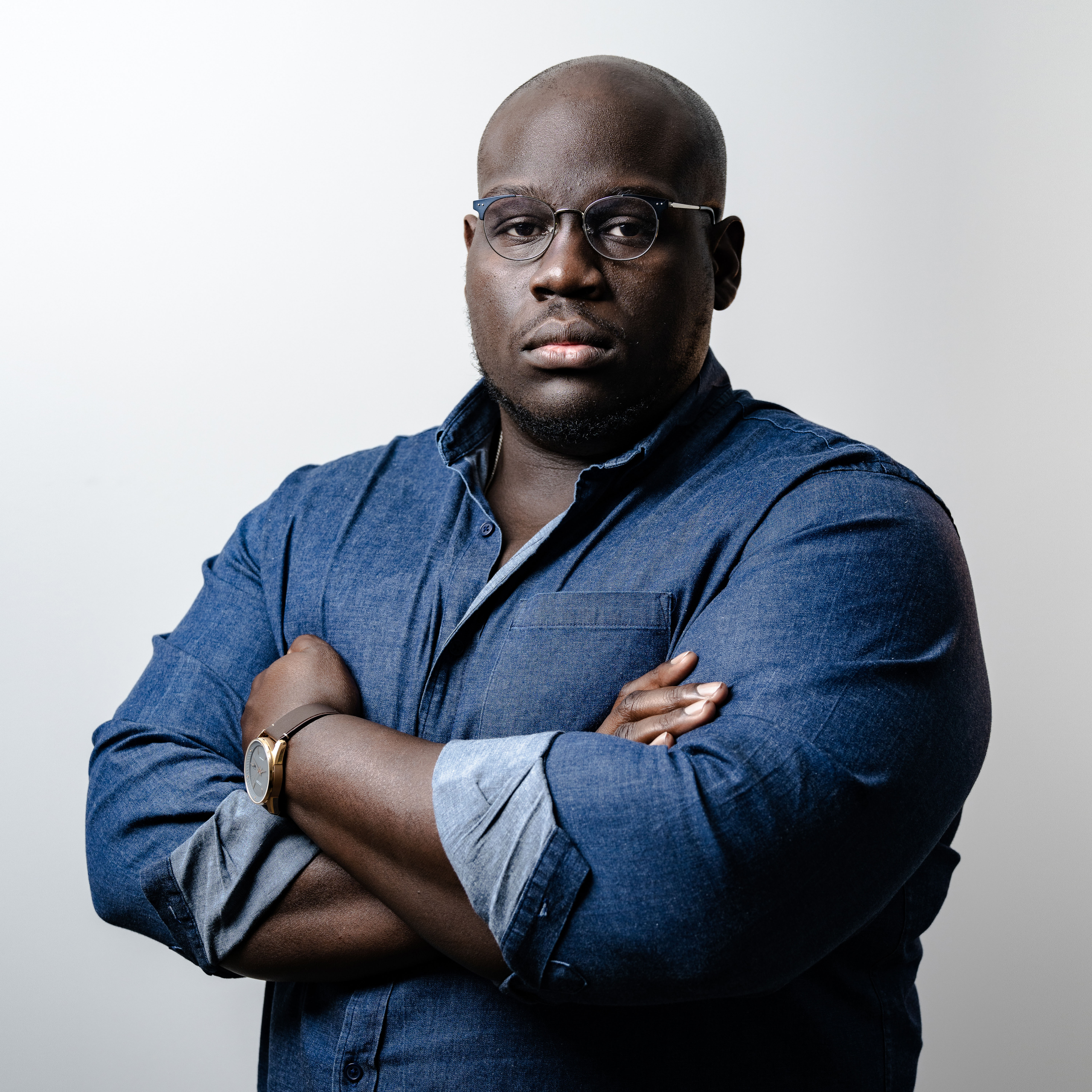 Color portrait of journalist and author Caleb Gayle. He is wearing a dark blue shirt and has his arms crossed.