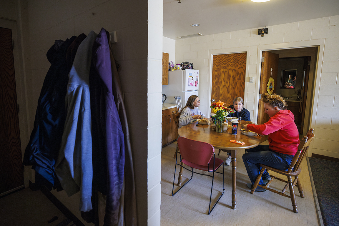 Three people sit together at a table to eat while their jackets hang in the forefront