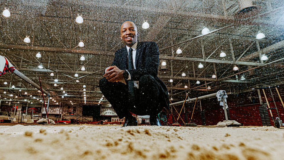 Nebraska's Passmore Mudundulu kneels at the edge of the jump pit in the Devaney Sports Center as sand rains down in front of the camera. Mudundulu is a junior marketing major from Lincoln.