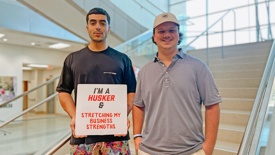 Rob Khorrom and Zach Molzer smile for a photo inside Hawks Hall with a sign that reads “I’m a Husker & stretching my business strengths”