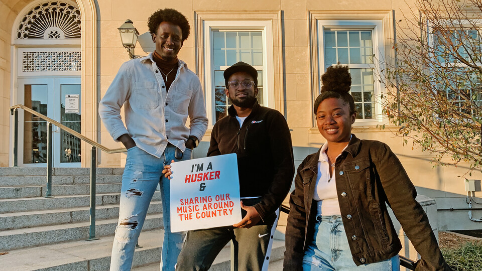 Live Lyve members (from left to right ) Japhet Ingeri, Benoit Kayigamba and Esther Uwamahoro pose in front of the Union. Kayigamba holds a sign that reads "I'm a Husker & Sharing Our Music Around the Country."
