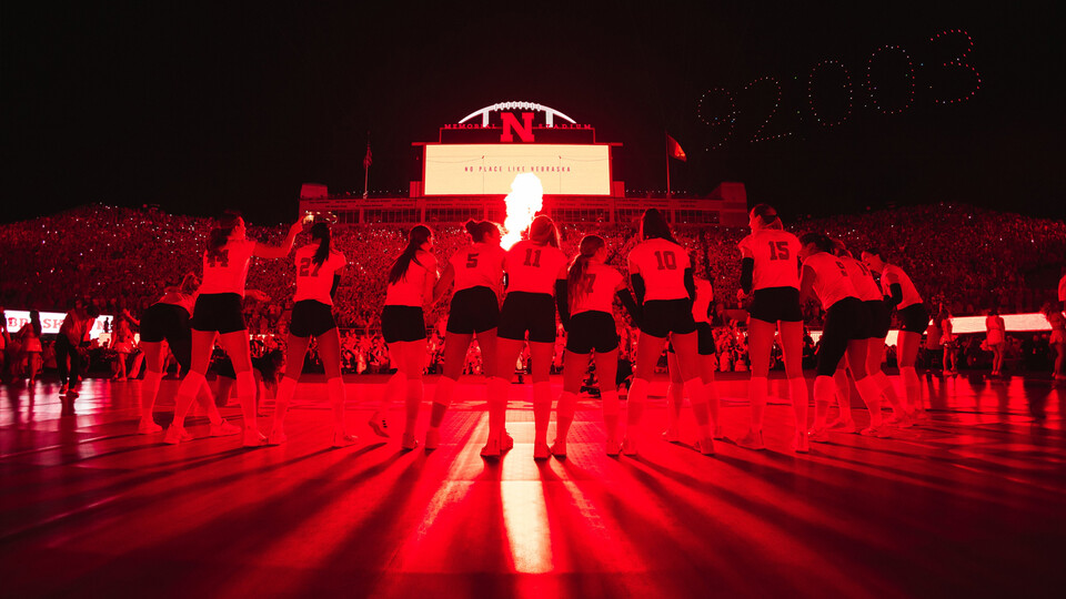 Red light bathes the Husker volleyball team as it celebrates a win in Memorial Stadium