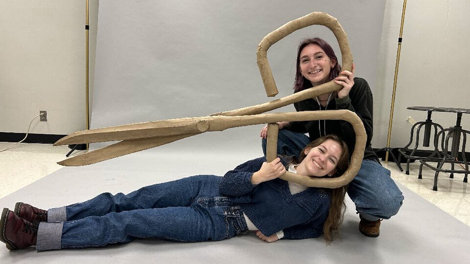 Husker students pose with an oversized pair of scissors fabricated from chipboard