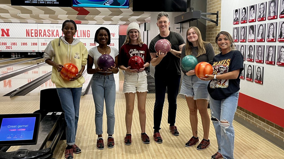 A group of Husker transfer students hold bowling balls while smiling for the camera