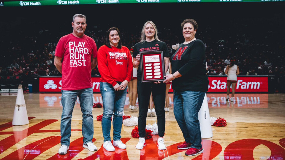 Allison Weidner and her family hold up a scholarship plaque while standing at midcourt in Pinnacle Bank Arena