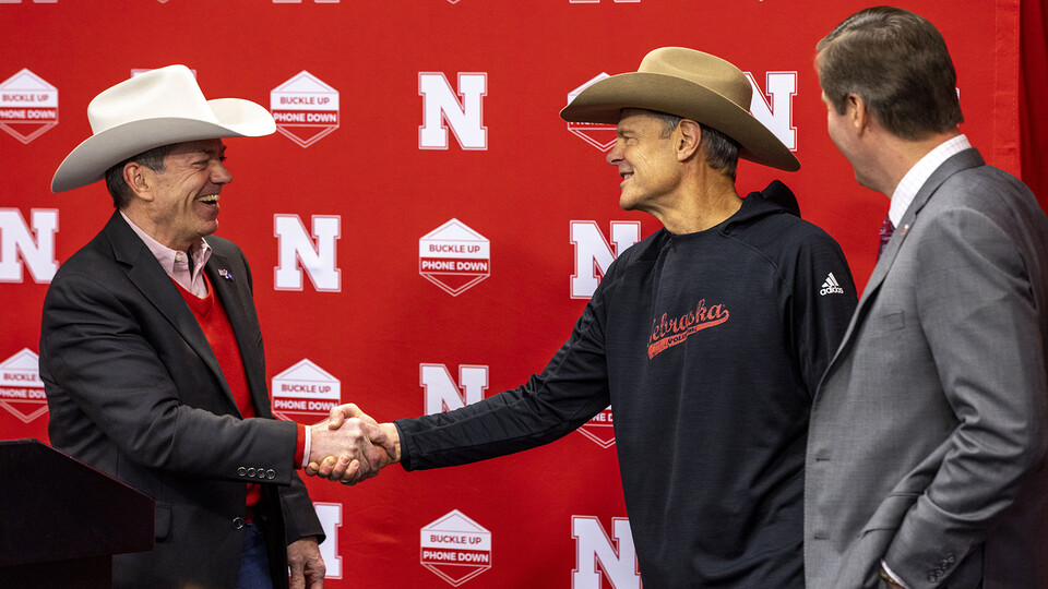 Gov. Jim Pillen (left) shakes hands with John Cook, Husker volleyball head coach, while Trev Alberts looks on. As part of his presentation at the Feb. 24 Volleyball Day in Nebraska announcement, Pillen gave Cook a cowboy hat.