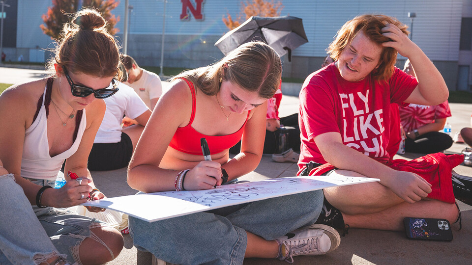 Husker fans craft signs while sitting on the sidewalk before Nebraska volleyball's match against Wisconsin