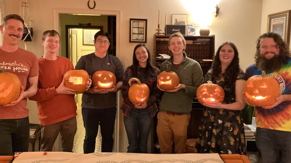 Husker graduate students hold their carved jack-o’-lanterns while smiling for the camera