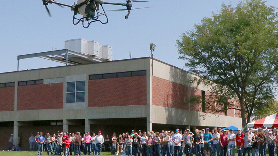 A crowd in the background looks on at an airborne drone in the foreground