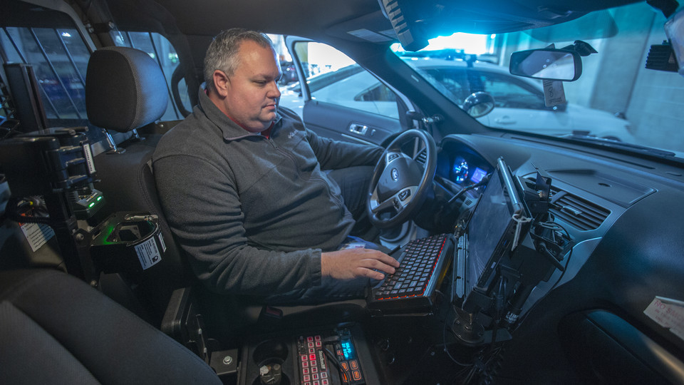 Sean Humphrey, IT manager for the University Police Department, examines a tablet computer in a cruiser. Eight information technology employees maintain the security systems used by university police.