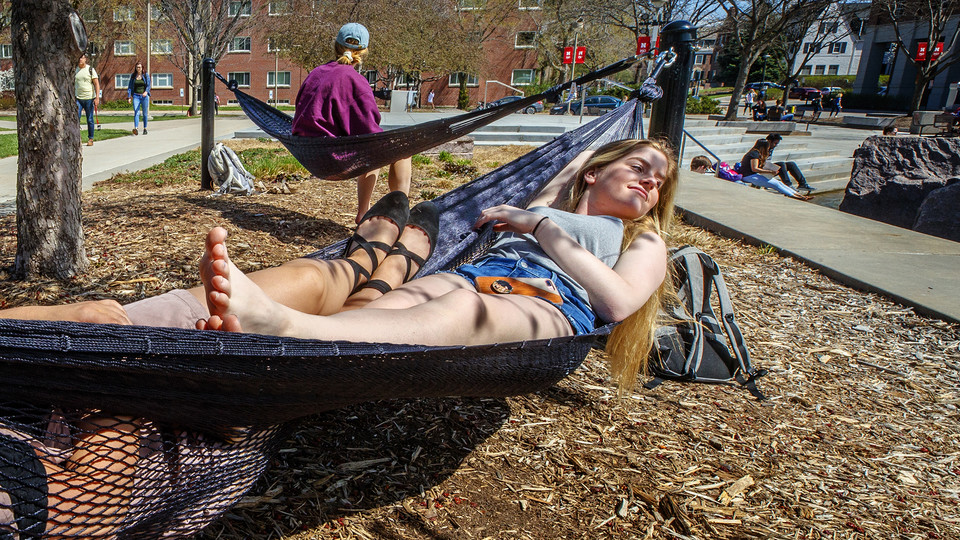 Music majors Sammy Cope and Calli Mah relax in the sun as they swing in a hammock by Broyhill Fountain on the plaza by the Nebraska Union. The university is offering a variety of stress-reducing activities and extended building hours during the final two weeks of the spring semester. Final exams start April 29 with commencement exercises on May 3-4.