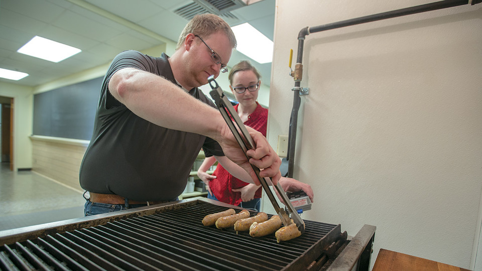 Nebraska's Gary Sullivan and Becca Furbeck prepare some of the jalapeño popper bratwurst on a grill in an animal science kitchen. The brats have twice earned a national taste test and are available for purchase on East Campus.