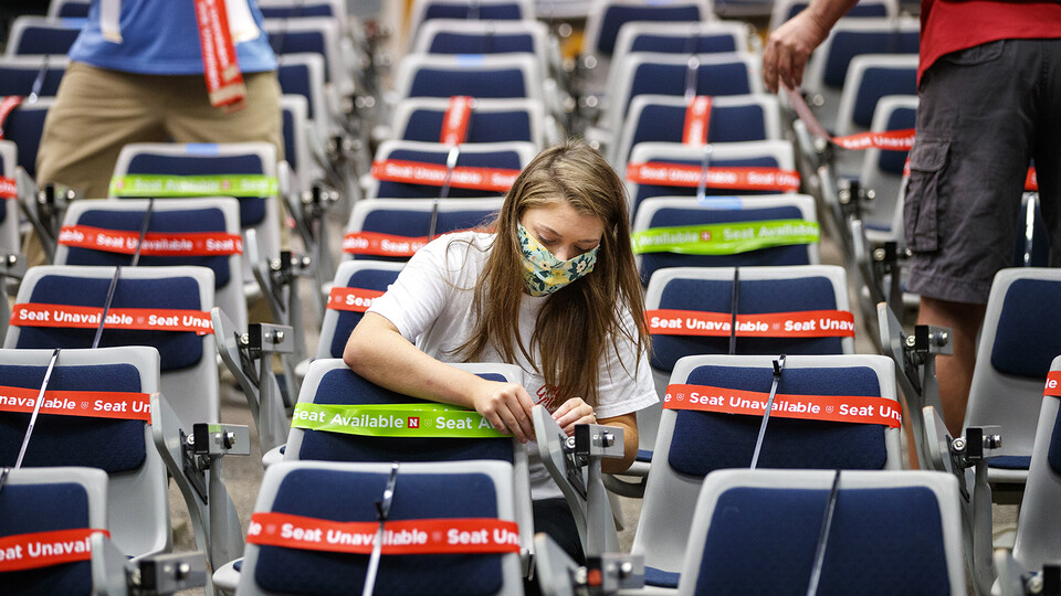 Maddie Huppert, a student worker in the Office of the Executive Vice Chancellor, wraps a green band on an available seat in a Louise Pound Hall lecture space. The bands are flexible so they do not need to be removed when the student sits down.