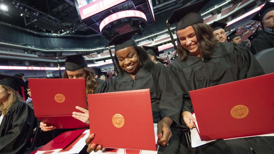 (From left) Julia Storm, Davetta Nelson and Gianna Astorino look over their diplomas in criminal justice during the summer all-university commencement ceremony Aug. 13 at Pinnacle Bank Arena.
