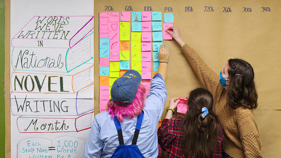 NaNoWriMo students — (from left) Wren Shawhan, Annie Lammes and Victoria Diersen — place sticky notes on the word-tracking board within the Writing Center.