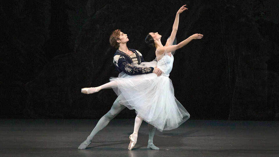 Male ballet dancer supporting female ballet dancer in white dress