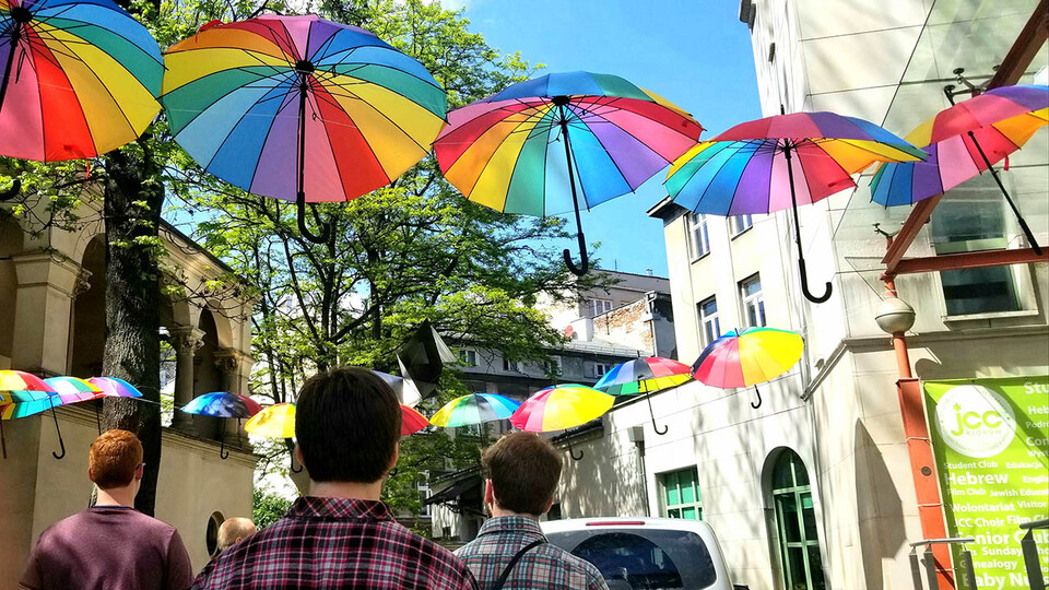 Group of young men walking down street with colorful umbrellas hanging overhead