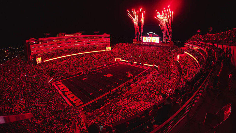 Memorial Stadium during night game, bathed in red light, with fireworks going off near north big screen