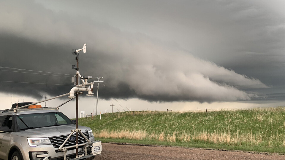A gray stormchasing SUV with instruments attached to the front and dark clouds behind