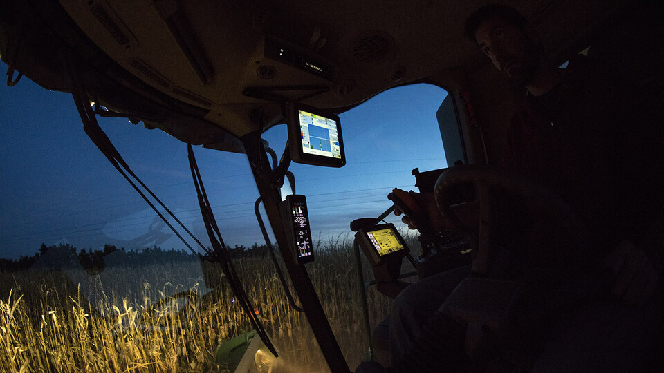 A man looks through the front windshield of a combine while harvesting corn at night.