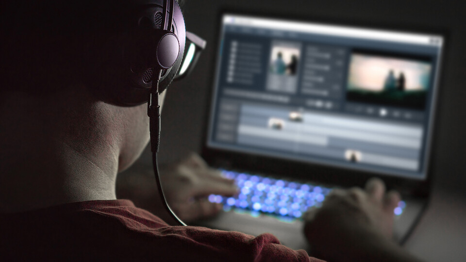 A young man wearing earphones edits video on a laptop