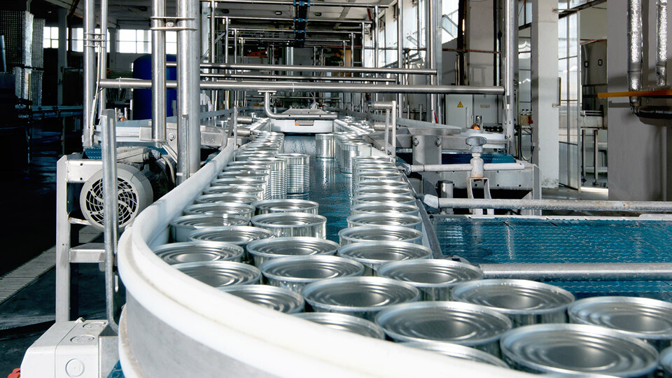 Metal cans move on a conveyor belt in a manufacturing plant.