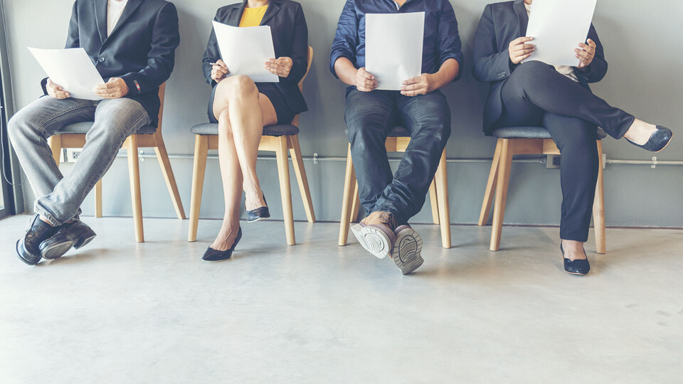 Legs of four job applicants sitting in chairs, holding resumes
