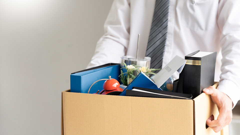 Man in shirt and tie carries cardboard box full of work belongings