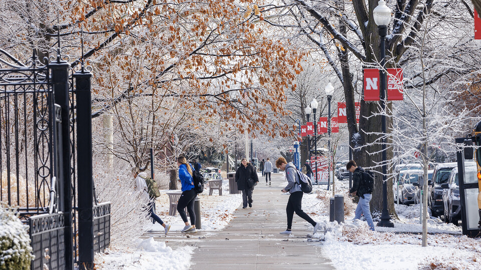 University of Nebraska–Lincoln students walk on a sidewalk near Louise Pound Hall, with snow covering the ground and tree branches.