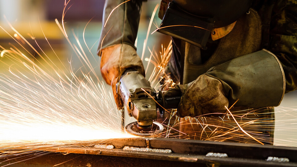 Sparks fly as a worker in protective gear uses a grinder on metal.